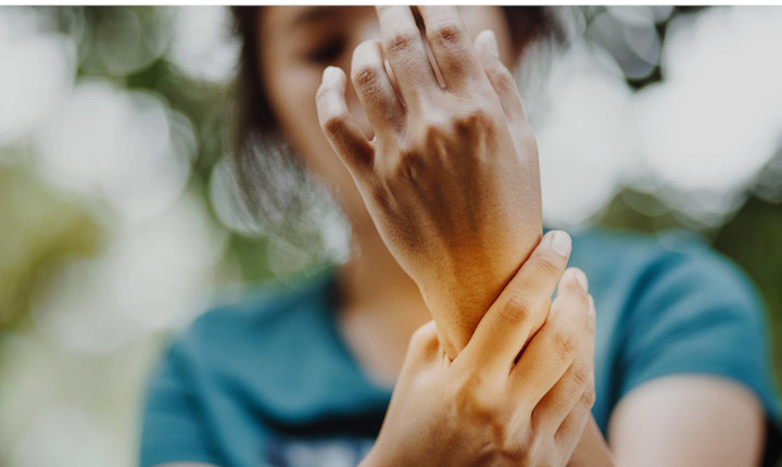 Woman in green t-shirt holding her wrist in pain