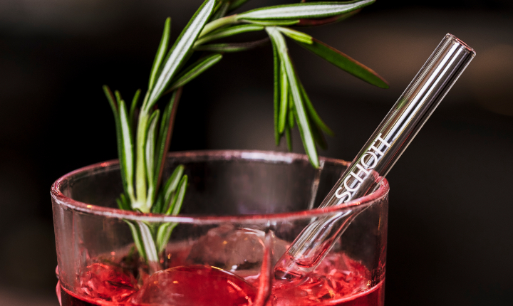 Glass straw in a drink of cranberry juice, ice and a sprig of rosemary