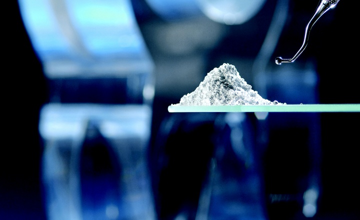 Pile of white powder dental glass on a glass slide in front of a glass tooth