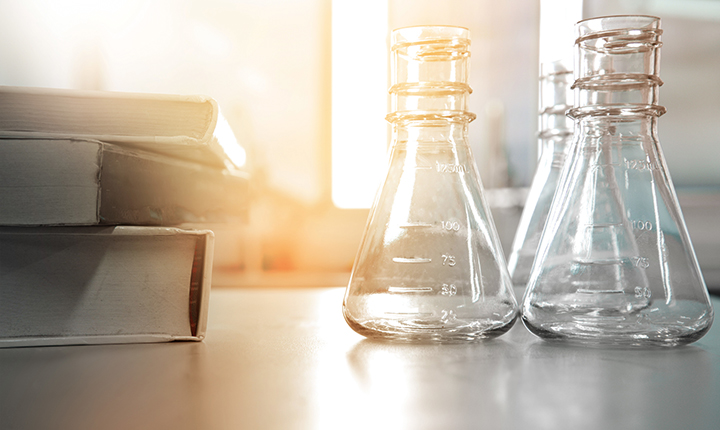 Three glass flasks in a science laboratory next to an education book