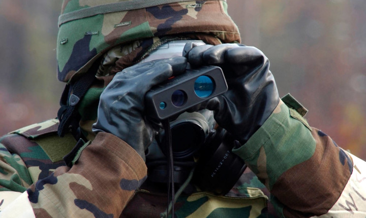 Solider in camouflage using a rangefinder to determine distance	
