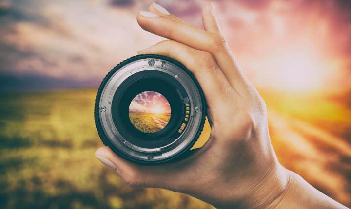 Hand holding a camera lens looking at a sunset	