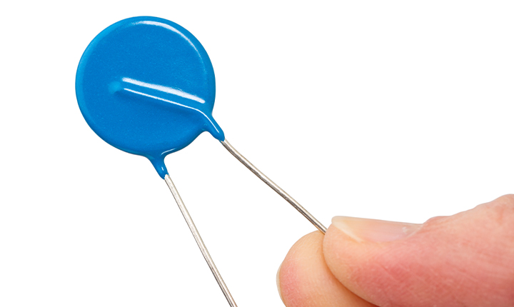 Two fingers holding a blue varistor