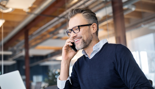 Man in glasses in business office on phone while working on laptop