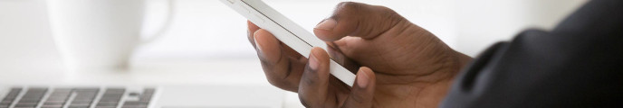 Hand holding a smartphone next to a laptop on a desk