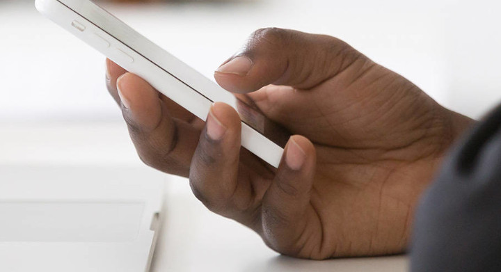 Hand holding a smartphone next to a laptop on a desk