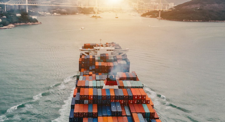 Full container ship traveling towards a sunset