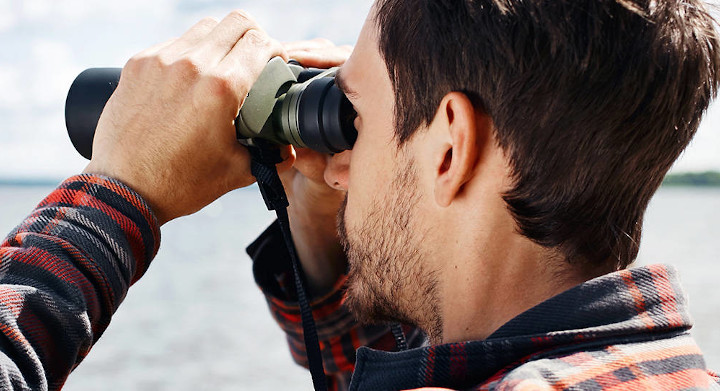 Many sports demand highly accurate sighting and rangefinding equipment Man looking through binoculars across lake