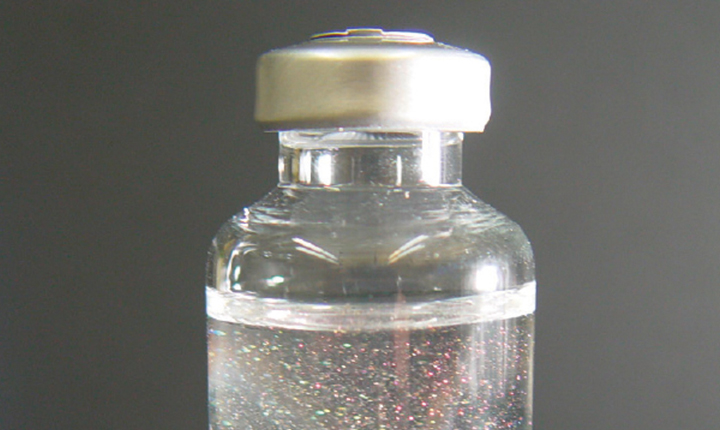 Sealed glass vial with clear liquid showing flake-like particles from delamination 