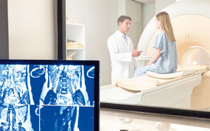 Male doctor talking to female patient sitting on MRI equipment in front of a display