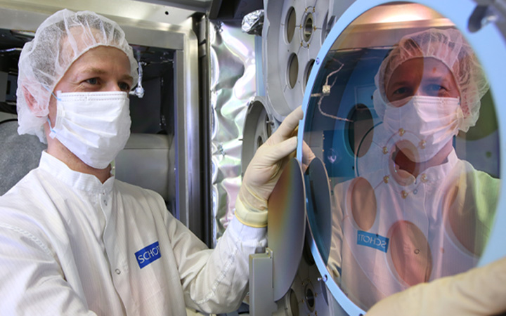 Scientist inspecting a large glass disc with optical coating