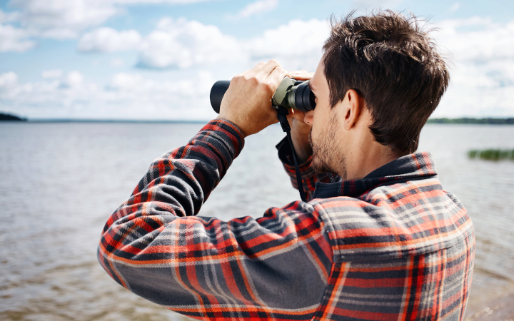 Man looking through binoculars across lake