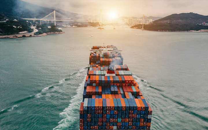 Full container ship traveling towards a sunset